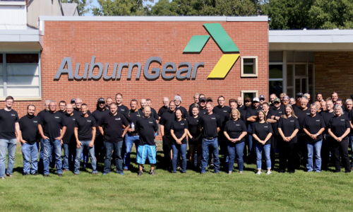 Group of people in matching black t-shirts outside AuburnGear, showing camaraderie and teamwork in a friendly atmosphere.