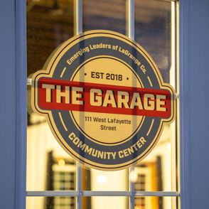 Sign for "The Garage" community center, established in 2018, framed by a window, evoking warmth and togetherness.