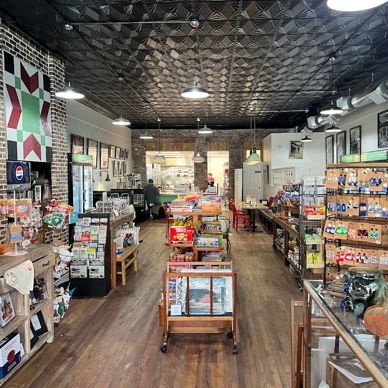 Warm, inviting store with wooden flooring and bright shelves filled with snacks, souvenirs, and local crafts, promoting comfort and curiosity.