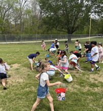 Children joyfully search for Easter eggs outdoors, holding colorful buckets in a vibrant, sunny, and grassy area.