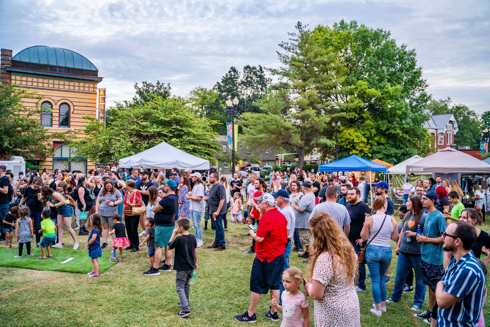 A vibrant outdoor event in a park with a large crowd, tents, and people of all ages enjoying community and celebration.