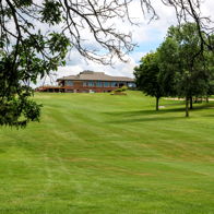 Serene landscape with lush grass, a large building, trees, and partly sunny clouds, evoking calmness and relaxation.