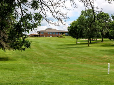 Serene landscape with lush grass, a large building, trees, and partly sunny clouds, evoking calmness and relaxation.