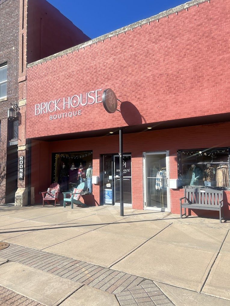 "BRICK HOUSE BOUTIQUE storefront with red brick façade, large display windows, cozy vibe, and benches for relaxation."