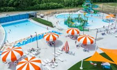 Vibrant water park with a blue pool, colorful slides, umbrellas, and people enjoying fun summer activities.