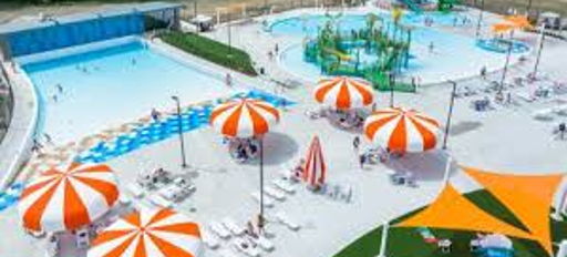 Vibrant water park with a blue pool, colorful slides, umbrellas, and people enjoying fun summer activities.