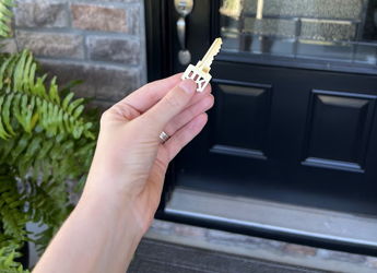 A hand holds a key in front of a welcoming door with a wreath, evoking excitement, warmth, and anticipation for new beginnings.
