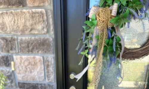 A hand holds a key before a welcoming, decorated front door, symbolizing new beginnings and opportunity.