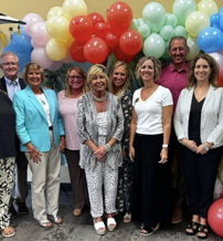 A joyful gathering of people in front of colorful balloons, celebrating together with smiles and festive attire.