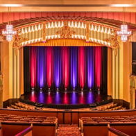 Theater interior with red and purple curtains, plush tiered seating, elegant lighting, evoking excitement and anticipation.