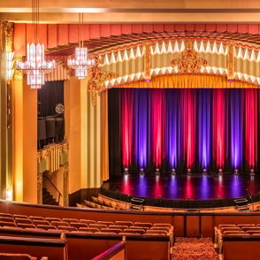 Theater interior with red and purple curtains, plush tiered seating, elegant lighting, evoking excitement and anticipation.