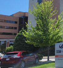 Modern healthcare facility "S2 Health" with American flag, green trees, and red vehicle under a bright blue sky.