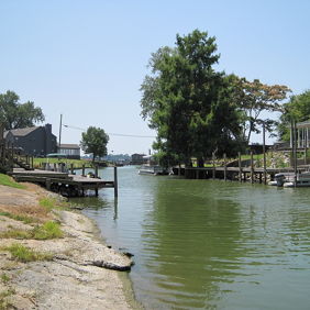 Serene waterway with greenery, wooden docks, and houses, evoking tranquility and a sense of peaceful outdoor leisure.