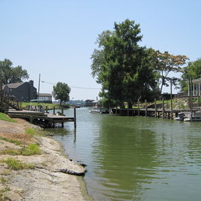 Serene waterway with greenery, wooden docks, and houses, evoking tranquility and a sense of peaceful outdoor leisure.