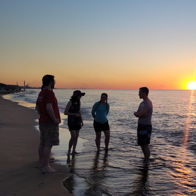 Four people chat by the beach at sunset, surrounded by warm hues, evoking tranquility, joy, and connection.