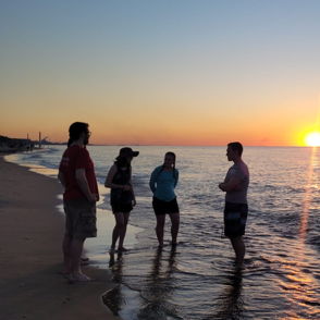 Four people chat by the beach at sunset, surrounded by warm hues, evoking tranquility, joy, and connection.