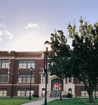 A classic brick school building surrounded by lush green lawn and trees, radiating warmth and tranquility in the sunlight.