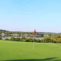 Serene golf course with a green fairway, calm water, and a red flag, evoking relaxation and a peaceful outdoor escape.