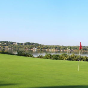 Serene golf course with a green fairway, calm water, and a red flag, evoking relaxation and a peaceful outdoor escape.