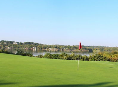 Serene golf course with a green fairway, calm water, and a red flag, evoking relaxation and a peaceful outdoor escape.