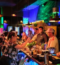 Lively bar scene with diverse patrons socializing under colorful neon lights, evoking excitement and camaraderie in a festive atmosphere.