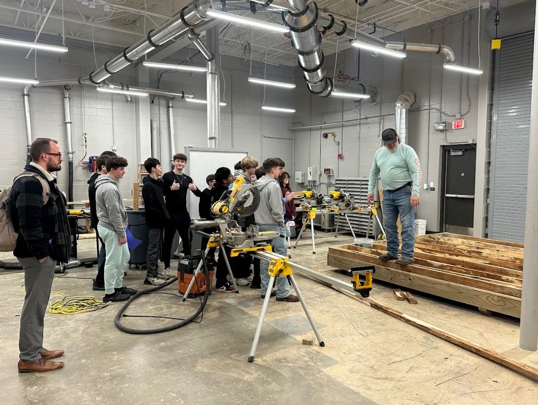 Students observe a demonstration in an industrial classroom, highlighting hands-on learning and engagement in practical education.