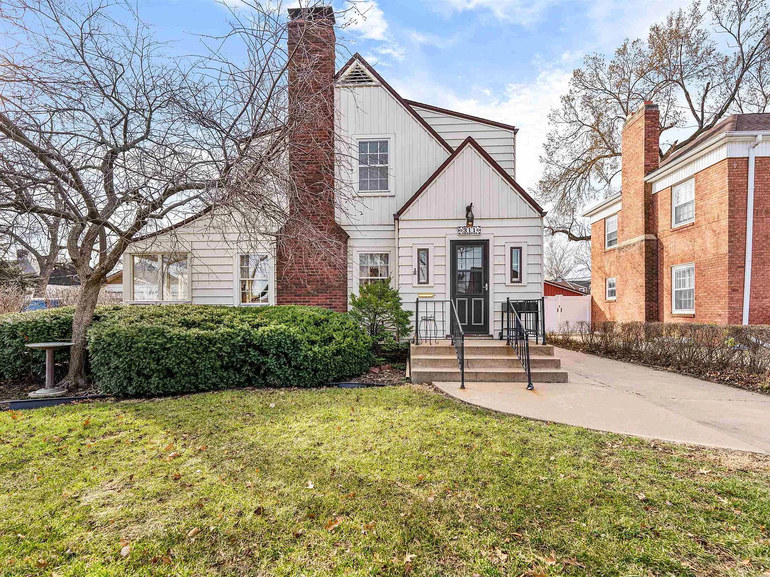 A charming house with white siding and brick, featuring a porch and manicured yard, evokes warmth and nostalgia.