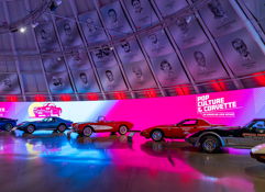 Vibrant exhibition space showcasing vintage Corvettes with dynamic lighting and pop culture graphics, evoking nostalgia and excitement.