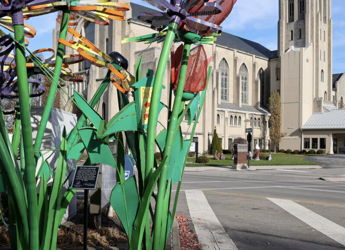 Vibrant oversized flower sculptures in bright colors contrast with a muted building, evoking joy and creativity in a lively setting.