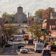 A charming small-town street with brick buildings, a church, autumn trees, active vehicles, and a warm, nostalgic atmosphere.