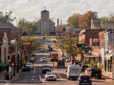 A charming small-town street with brick buildings, a church, autumn trees, active vehicles, and a warm, nostalgic atmosphere.