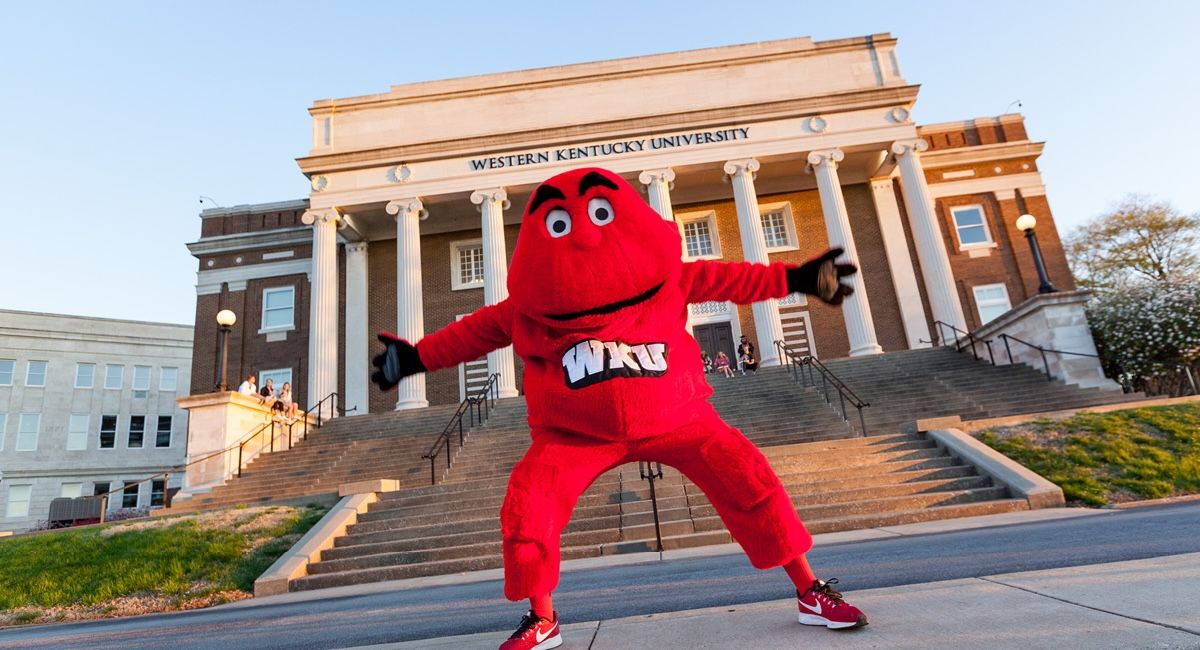 A lively red mascot poses in front of a university building, conveying school spirit and enthusiasm at Western Kentucky University.