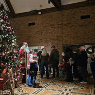 A festive indoor scene features a decorated Christmas tree, cozy couch, and a joyful group waiting to meet Santa.