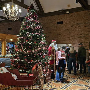 A festive indoor scene features a decorated Christmas tree, cozy couch, and a joyful group waiting to meet Santa.
