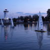 A serene evening scene with a lighthouse, sailboats, and a calm water reflection under a twilight sky of blues and purples.