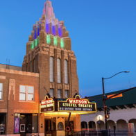 Vintage theater with art-deco design, colorful spire, and marquee, evoking nostalgia and excitement under a twilight sky.