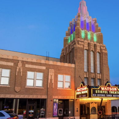 Vintage theater with art-deco design, colorful spire, and marquee, evoking nostalgia and excitement under a twilight sky.