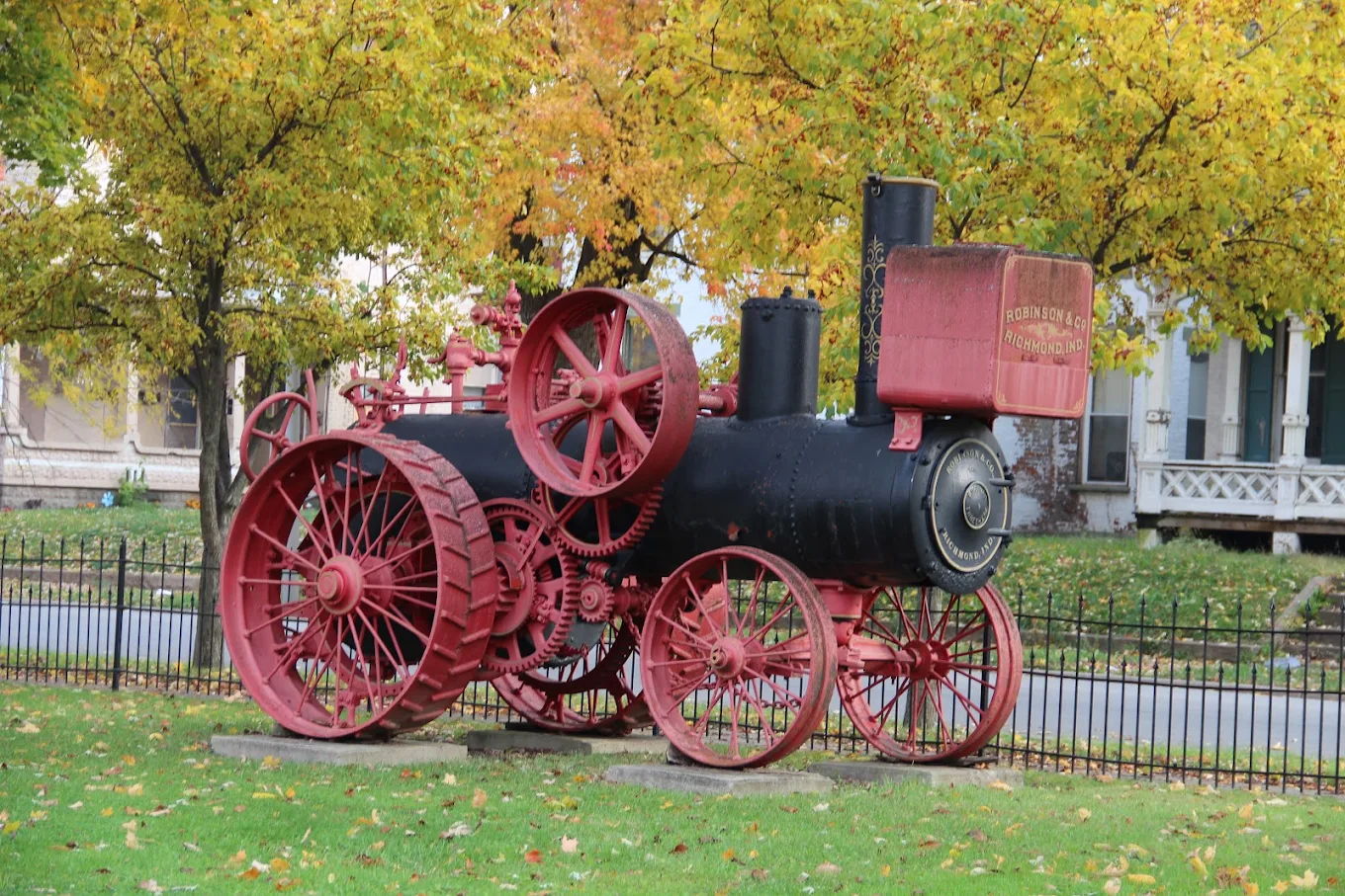 A vintage steam tractor in red and black stands among vibrant autumn trees, evoking nostalgia and appreciation for history.