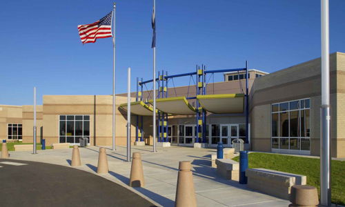 Modern educational building with vibrant design, colorful accents, flagpoles, and landscaped greenery, evoking positivity and community.