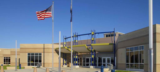 Modern educational building with vibrant design, colorful accents, flagpoles, and landscaped greenery, evoking positivity and community.