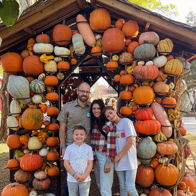 Family happily poses with pumpkins at a fall festival, enjoying a joyful moment together in a cozy outdoor setting.