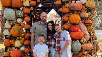 Family poses happily under a pumpkin-decorated canopy, exuding warmth and autumn joy at a festive outing.