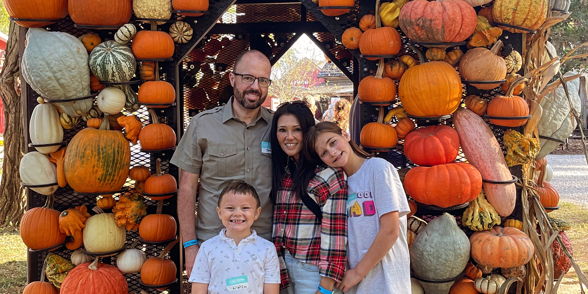 Family poses happily under a pumpkin-decorated canopy, exuding warmth and autumn joy at a festive outing.