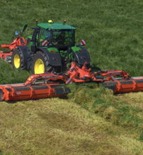 A green tractor with yellow wheels mows grass in a lush field, showcasing agricultural productivity and a vibrant landscape.