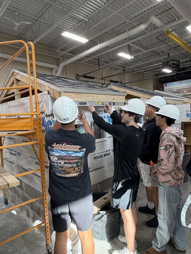 A group collaborates on a construction project indoors, showcasing teamwork and focus, wearing hard hats and engaged in learning.