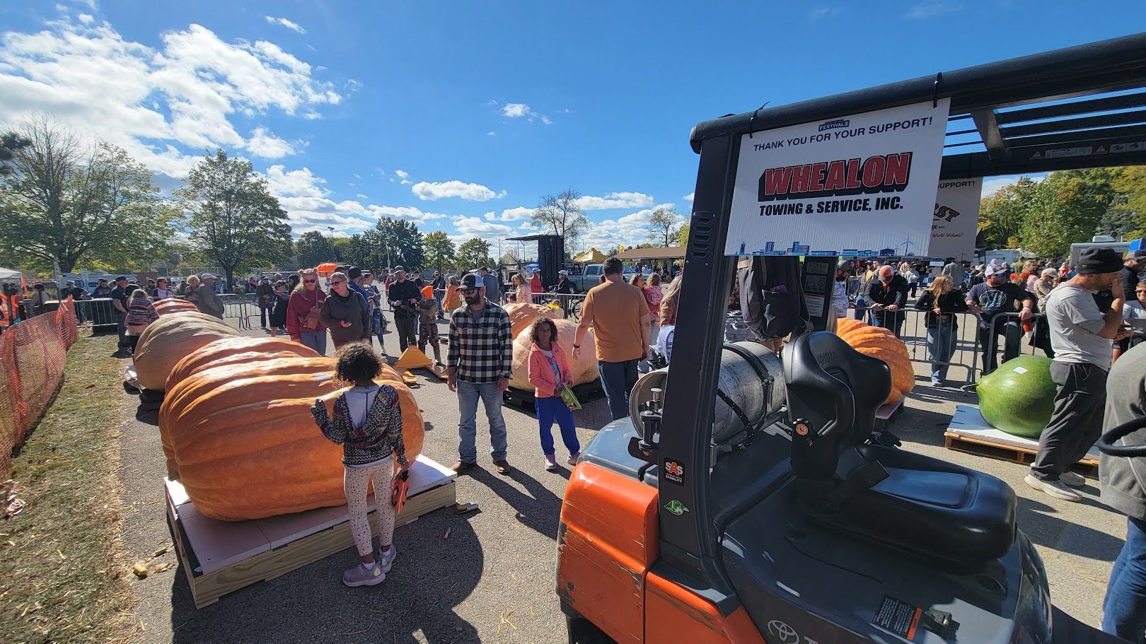 Lively pumpkin festival scene with large pumpkins, cheerful people, and a bright blue sky, evoking joy and community spirit.