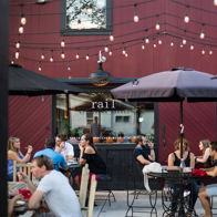 Outdoor dining scene with people, shaded umbrellas, string lights, and beautifully presented dishes, evoking joy and relaxation.
