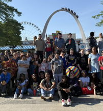 A lively outdoor group photo shows people smiling together near a ferris wheel, capturing joy, community, and excitement.
