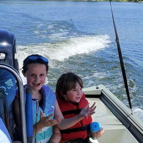 Two happy children in life jackets play in a small boat on a serene water body, evoking joy and adventure.
