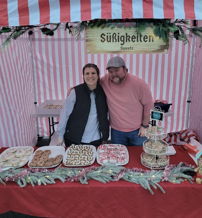 Festive sweets stand with a man and woman, cheerful decor, and baked goods, evoking warmth and joy in a market setting.